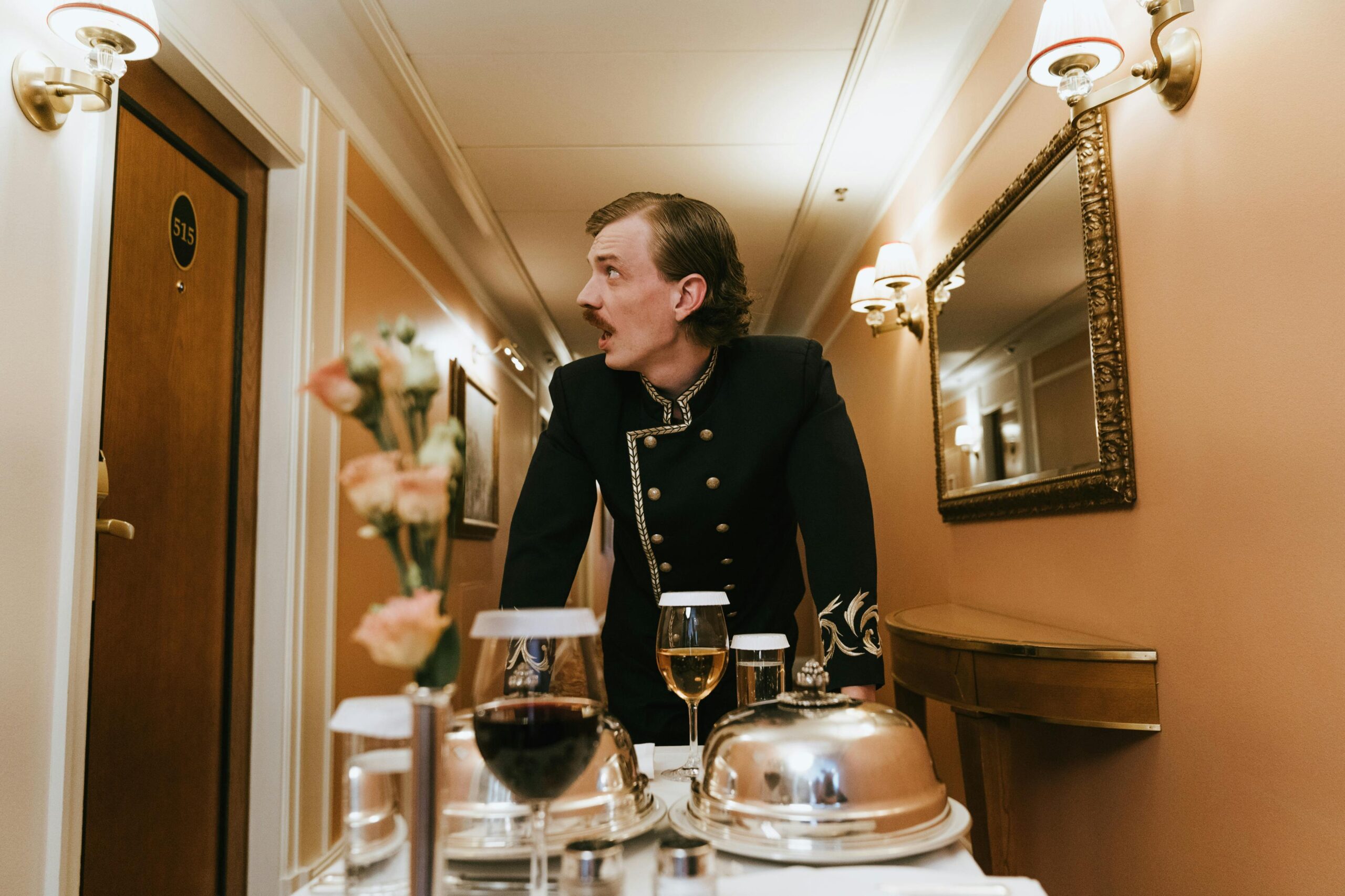 Hotel porter in vintage uniform delivering room service in a luxurious hallway.